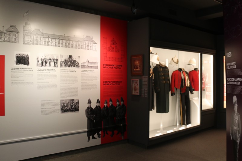 Image showing the gallery space with vinyl on the wall with text and images and a case with multiple uniforms. 