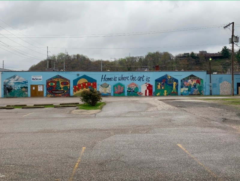 A mural faces a small empty parking lot on the back of a one-story building.