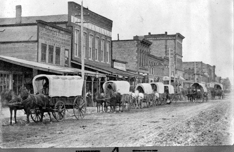 1870s-early 1880s photo of wagon train along Massachusetts St. - Old Liberty Hall behind pole (KSHS)