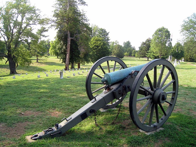 A cannon representing where Confederate General James Longstreet's cannon were located with his men in front along the stone wall. Headstones of the cemetery can be seen in the background. This section is called "Longstreet's Line."