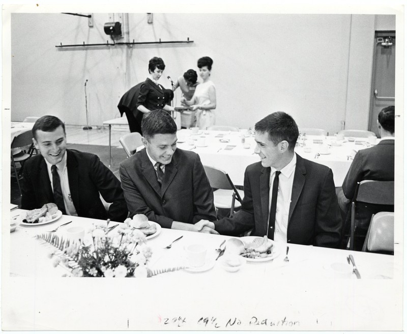 Black and white photograph of University of Oregon Medical students, Mike Moon, Peter Jensen and Dave Schwartz sitting at a banquet table in the student activities building.