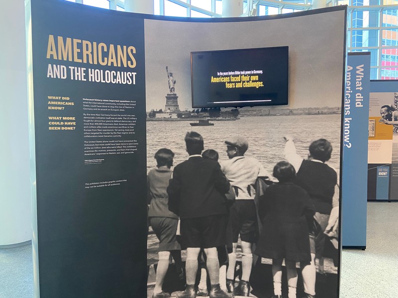 Black and white photo of young Jewish children on a boat pointing to the Statue of Liberty with the text "Americans and the Holocaust"