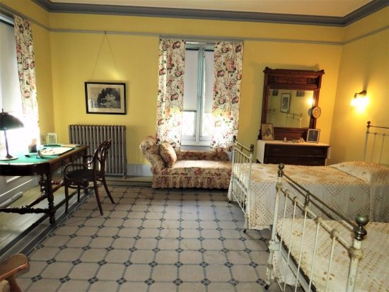 A view of a bedroom. The walls are painted a bright yellow. Furniture includes two white wrought-iron beds, an oak dresser with attached mirror, and a floral-patterned sofa. 