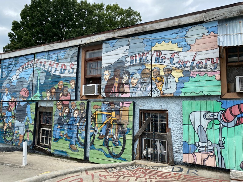 A large mural on the side of a building is painted with lots of activities surrounding biking.