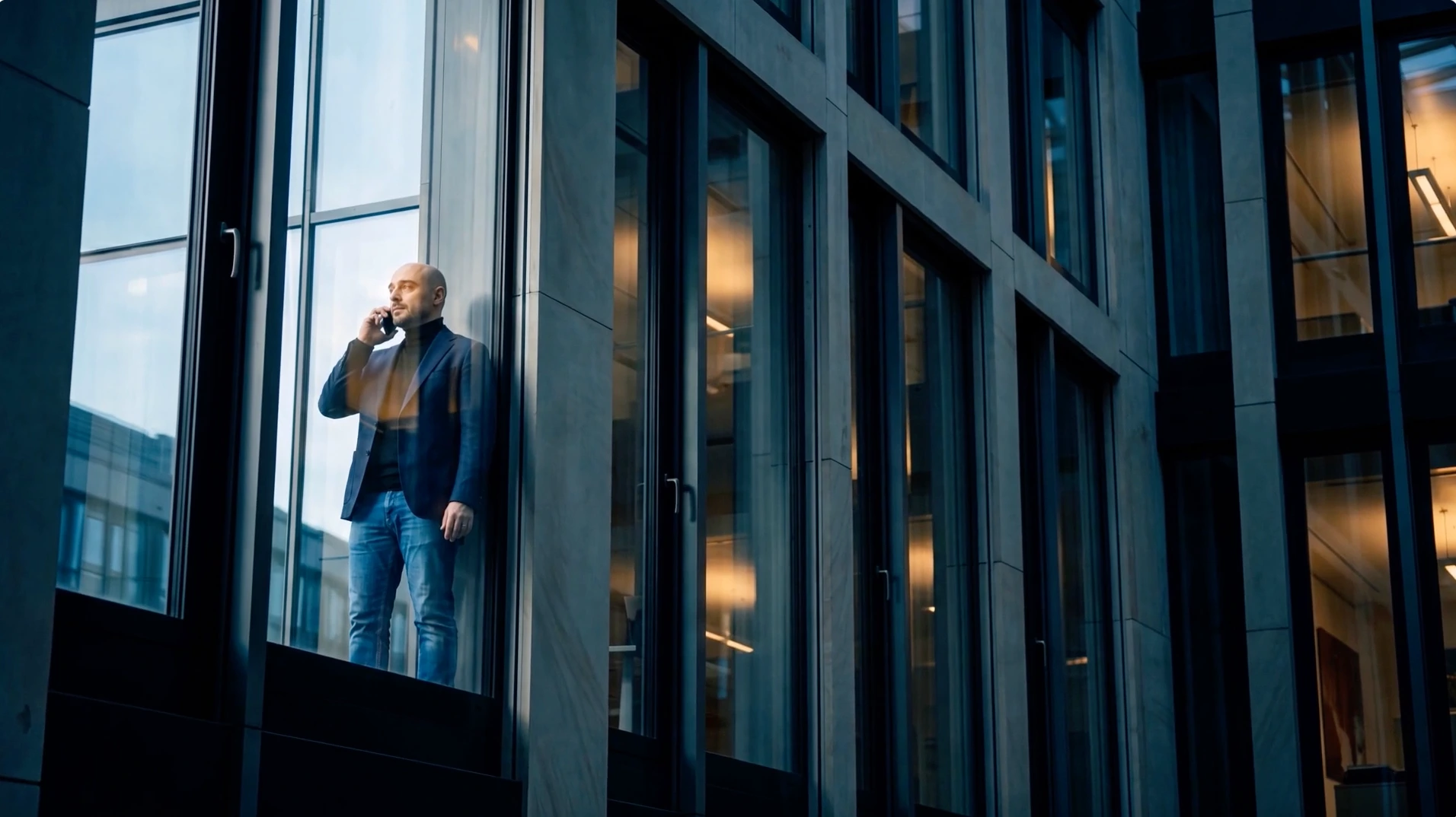 HRS Hybridfilm: ein Mitarbeiter telefoniert am Fenster, gesehen durch die Glasfassade.