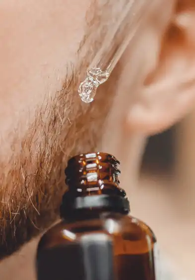 Close-up of a drop of beard oil being dispensed from a bottle, ready to be applied for beard care.