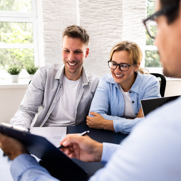 A man and woman, both real estate brokers, are seated at a table reviewing documents on a clipboard.