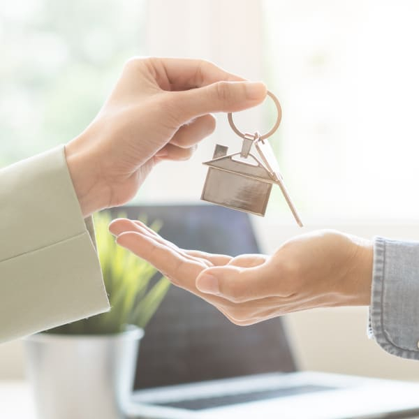 A real estate broker hands over a key to a new homeowner, symbolizing the transition to homeownership.