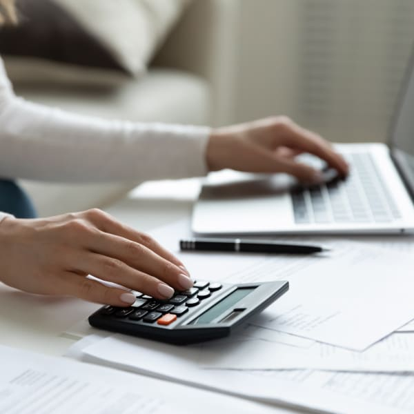 Femme utilisant une calculatrice et un ordinateur portable sur un bureau, réfléchissant à une maison à louer avec option d'achat.