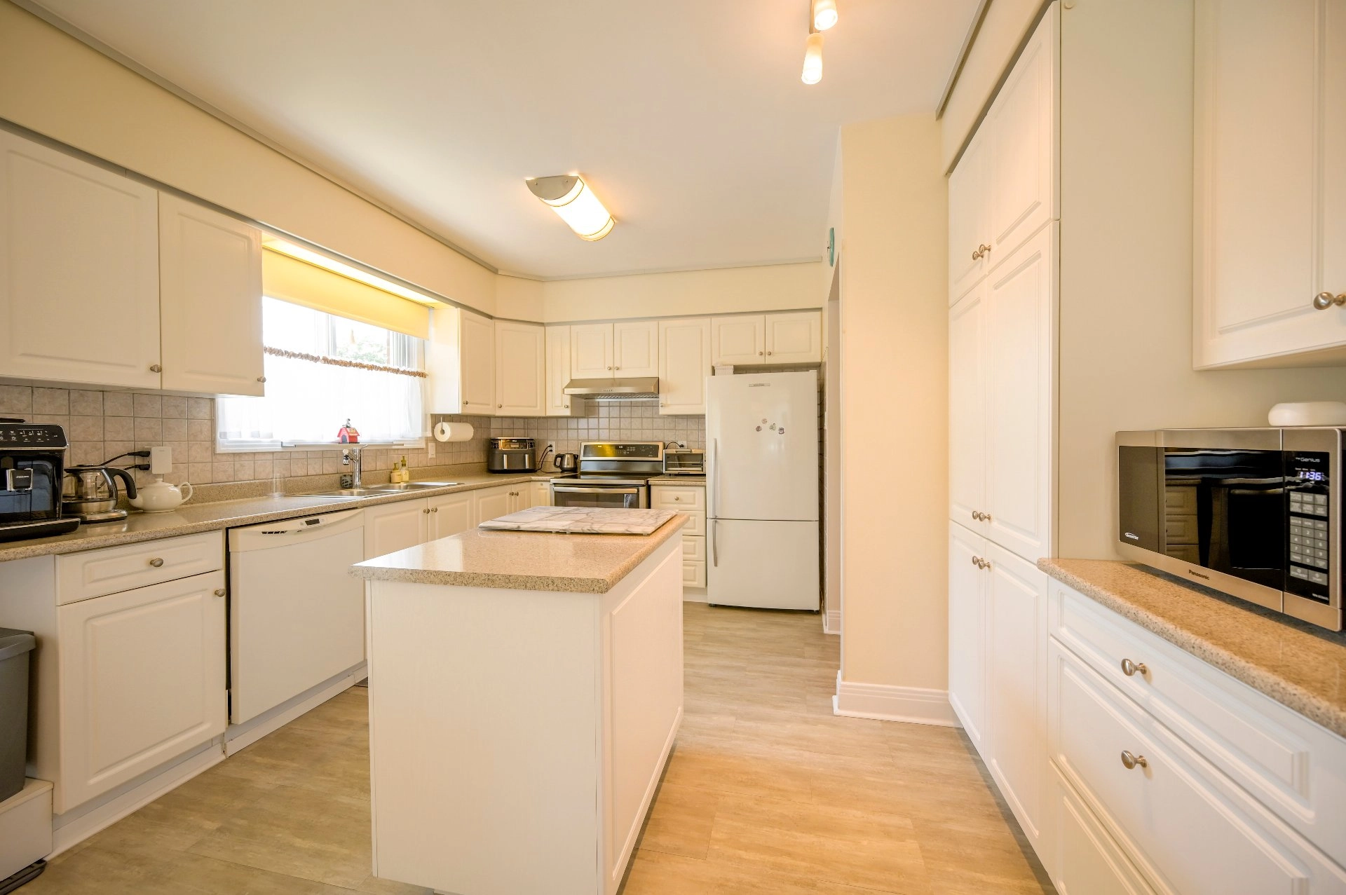 Spacious modern kitchen with white cabinets and large window.