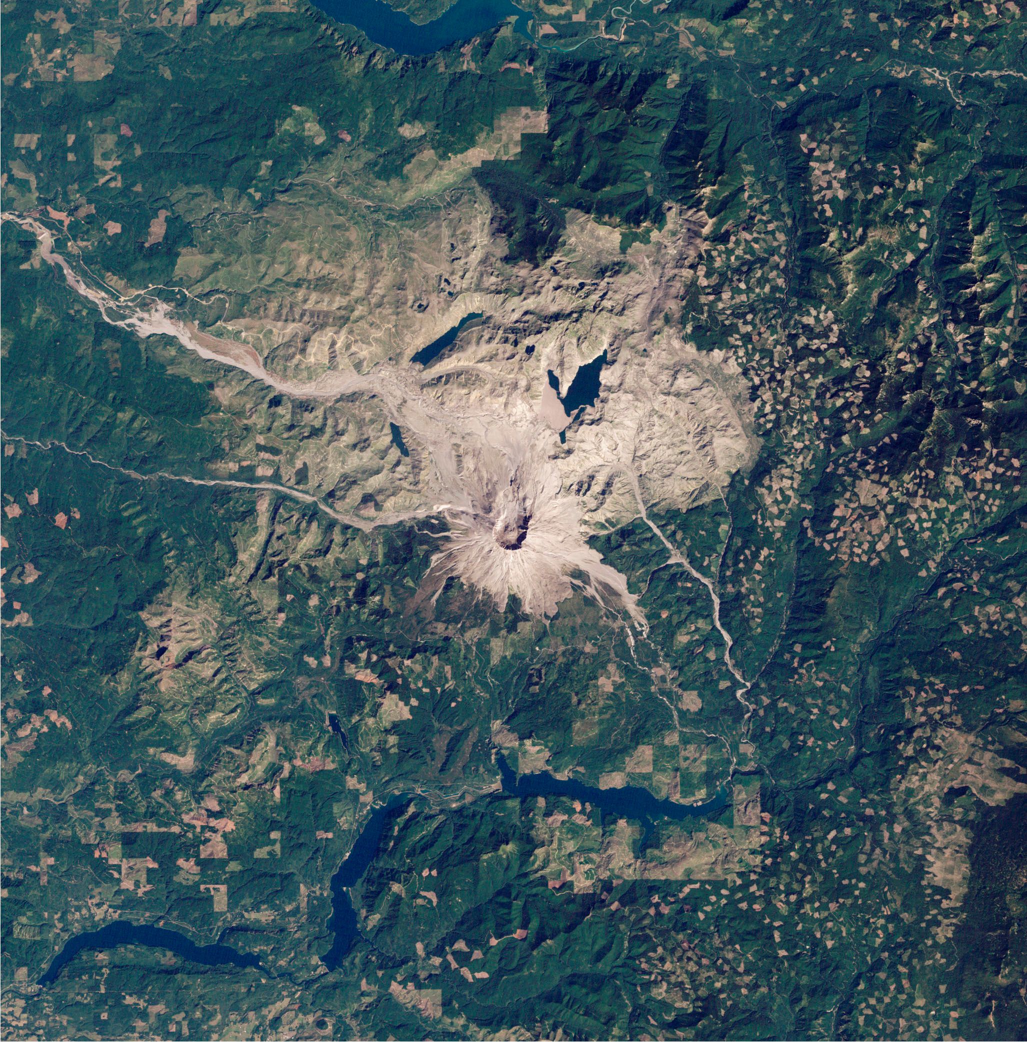 Rund um die grau-braune Vulkanlandschaft des Mount St. Helens ist eine grüne Landschaft zu sehen, oben und unten im Bild sind Stauseen sichtbar.