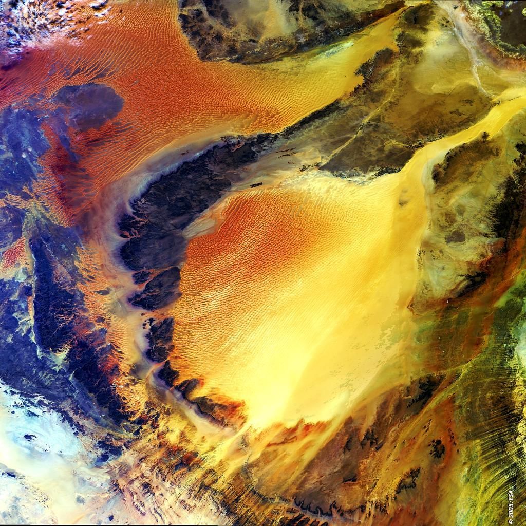 Die Dünen der Fezzan-Region sind rötlich eingefärbt, das dazwischenliegende Sandgestein hat eine dunkle Färbung.