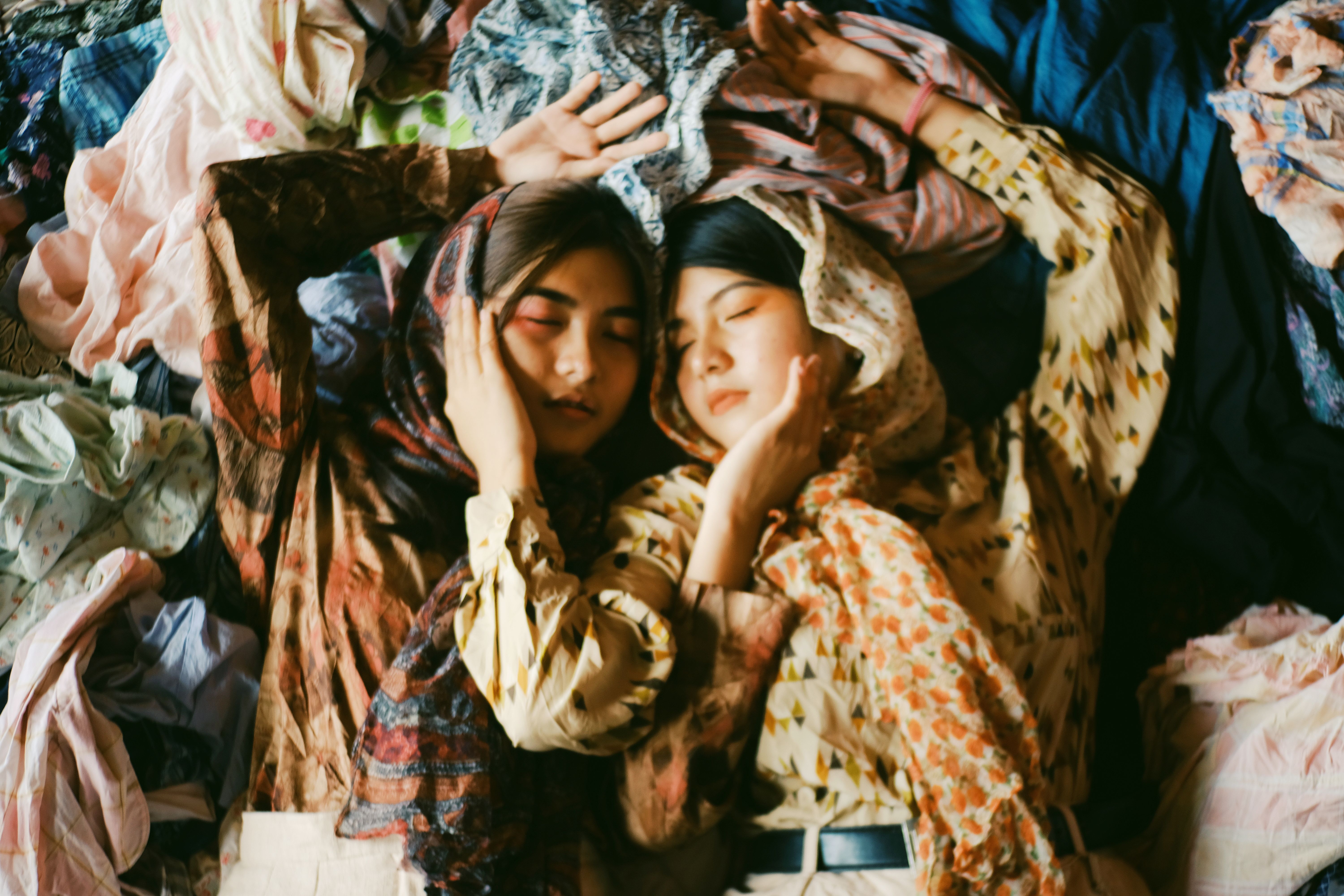 Free Two Women Wearing Earth-toned Printed Tops And Scarves Lying On A Pile Of Clothes Stock Photo