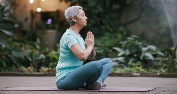 side view of woman with gray hair seated on a yoga mat with legs crossed