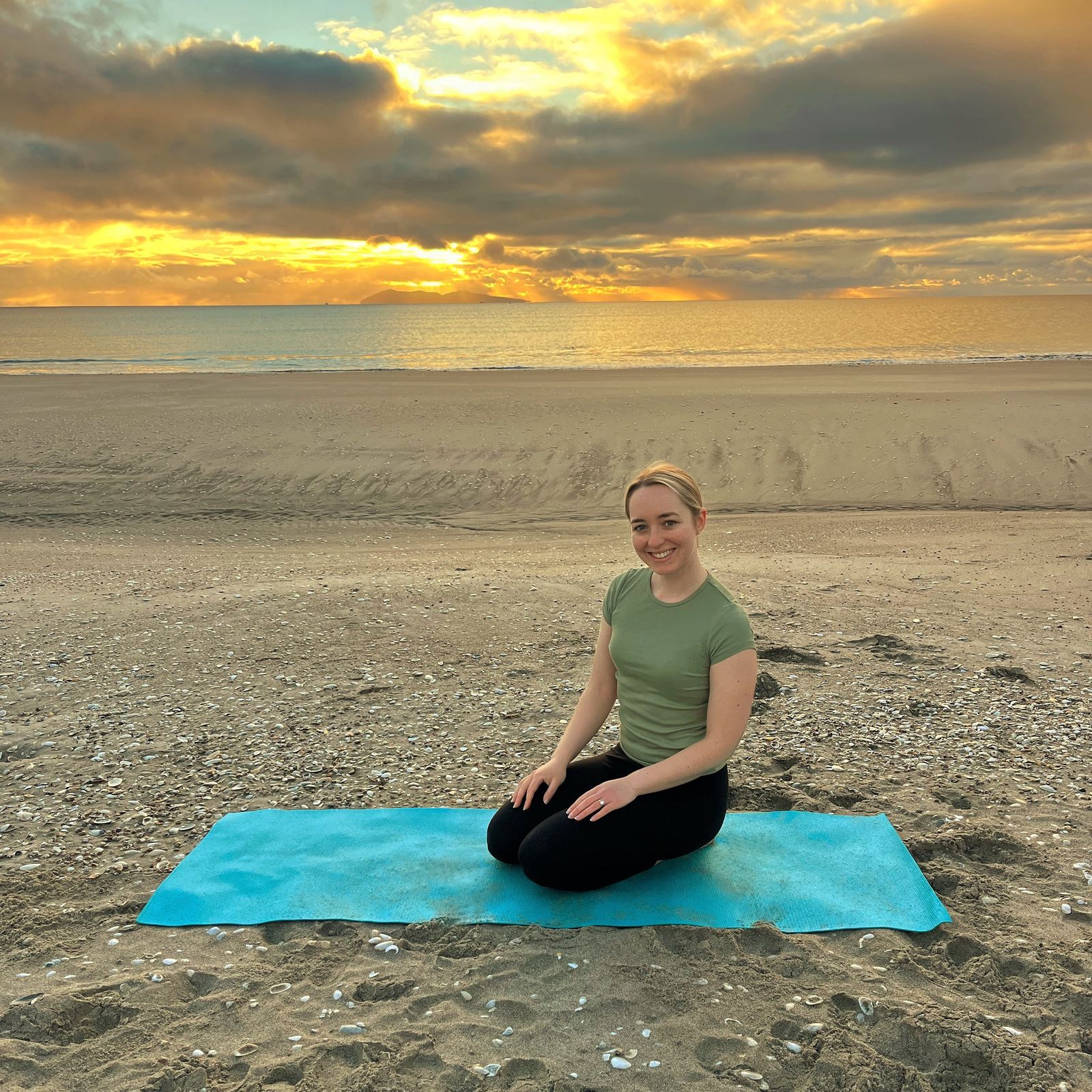 Ever Balance founder Harriet sitting on a mat at the beach, promoting online Pilates in New Zealand
