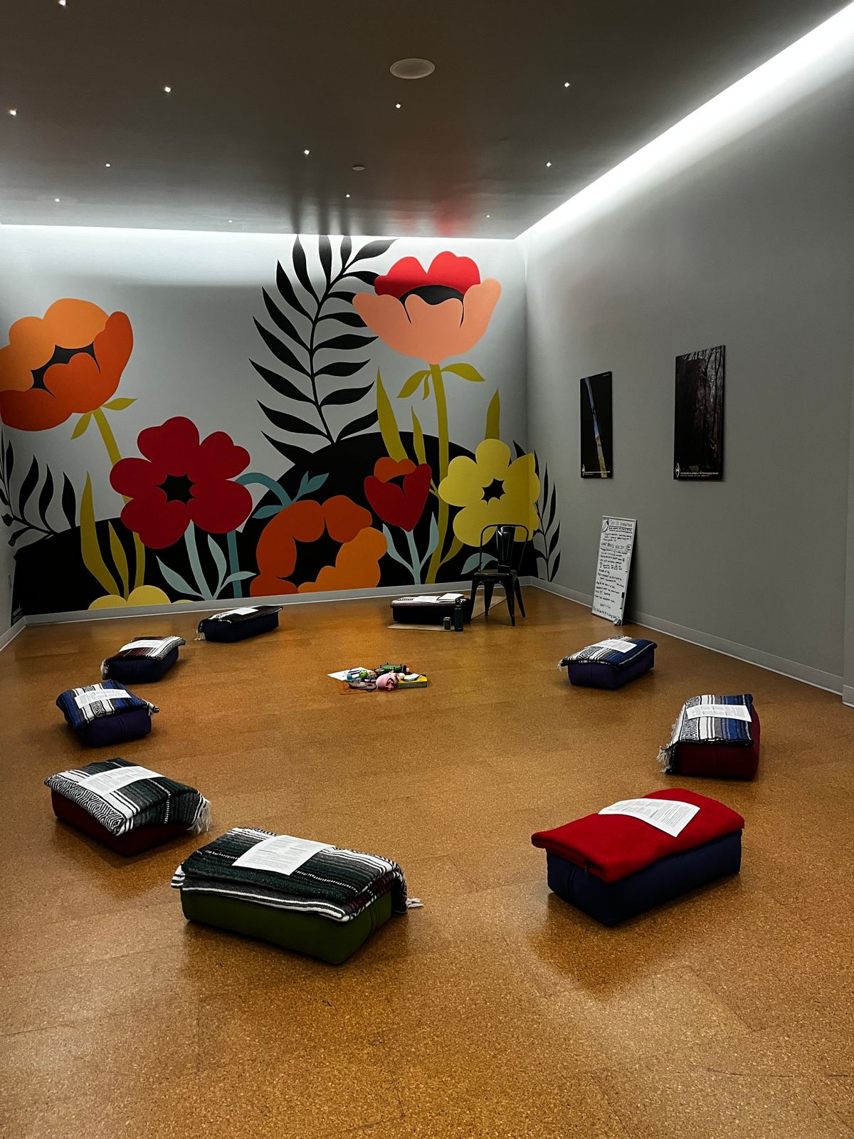 Photo of a yoga studio room with a colorful poppy mural on one wall, and starry lights on the ceiling. Yoga props are set up in a circle, ready for students to arrive.