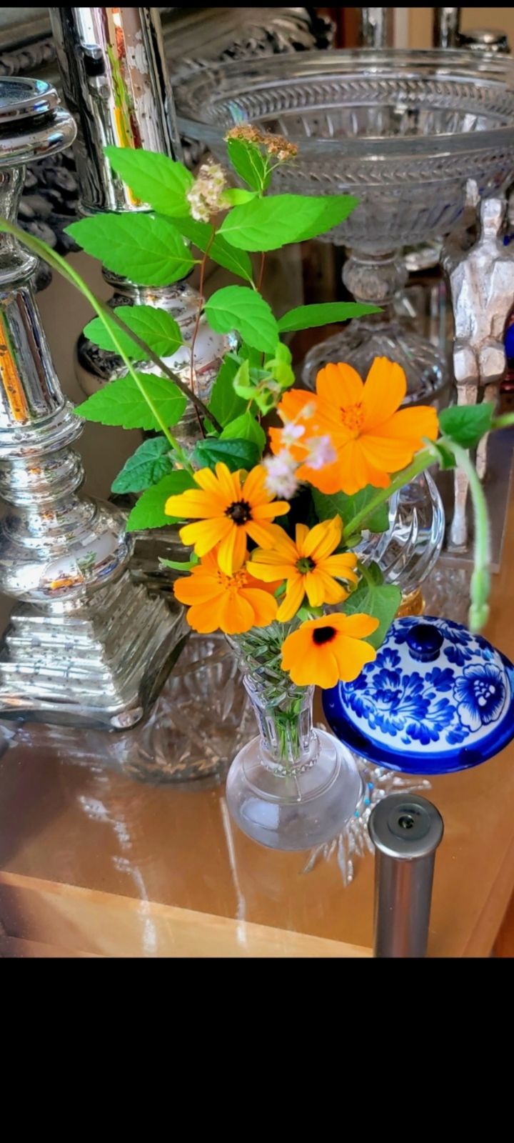 Cut Cosmos flowers and black eyed Susans in a vase on a shelf with other glass pieces