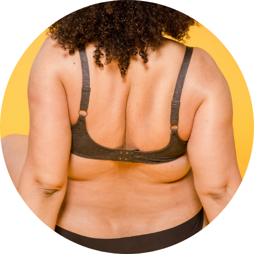 Unknown person sits away from camera.  We see long curly hair. They're wearing a bra and underwear, in a bigger body. 