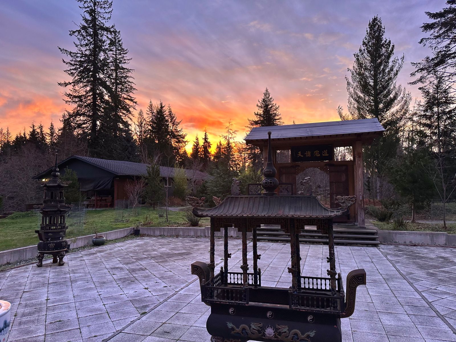 Sunrise over the Daoist temple courtyard and retreat center at Xuan Xiu Gong monastery. Entrance gate and incense burners are lit by the orange light of dawn.  The perfect place for qi gong, tai chi, and meditation practice during frequent Taoist retreats.