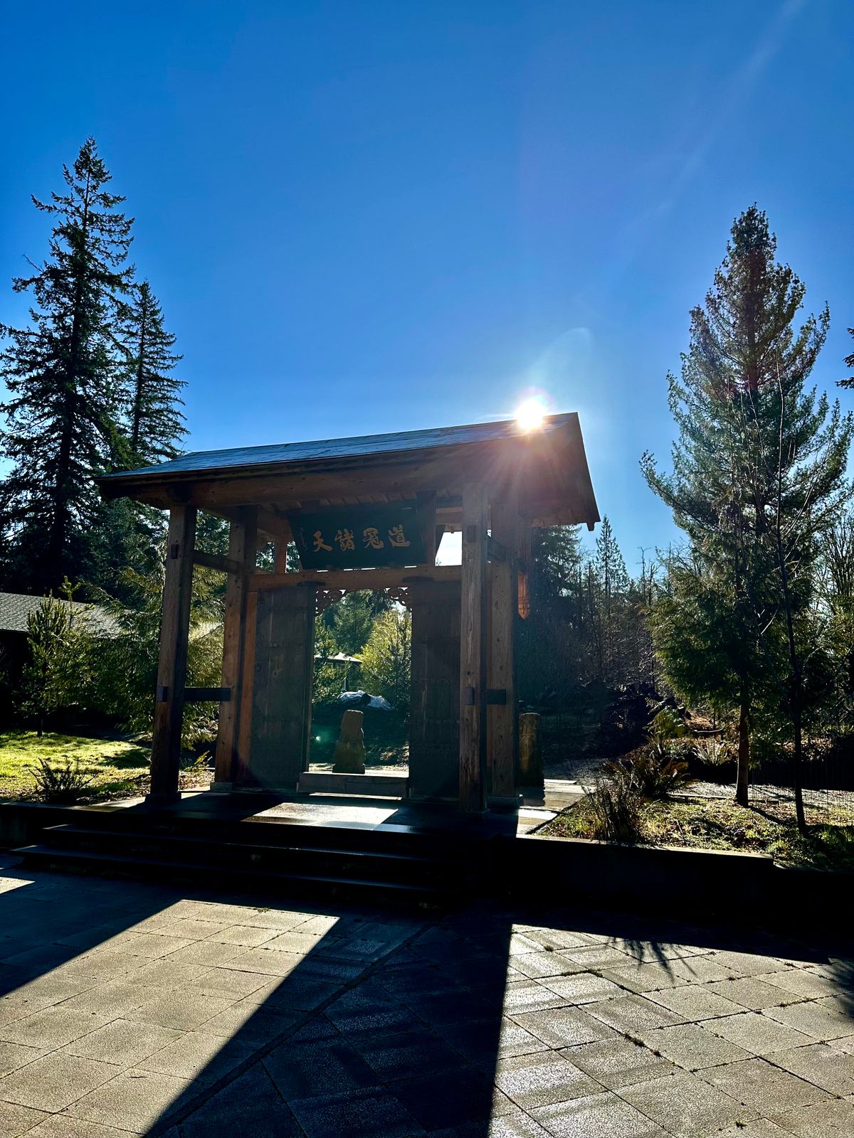 Midday winter sunlight shines above the entrance gate for the Daoist temple at Xuan Xiu Gong Taoist Sanctuary and retreat center, casting long shadows across the courtyard. The perfect place for qi gong, tai chi, and meditation practice during frequent Taoist retreats.