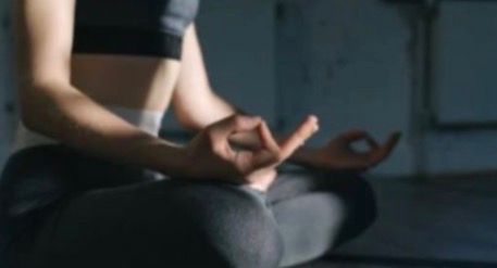 Woman sitting crossed legged on floor with hand Mudra in quiet accessible pose in a Yin Yoga session