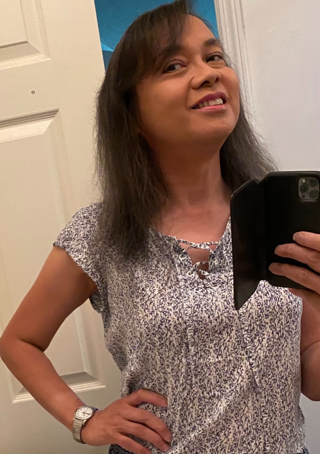 A woman takes a selfie in front of a mirror. She is smiling and wearing a patterned shirt.