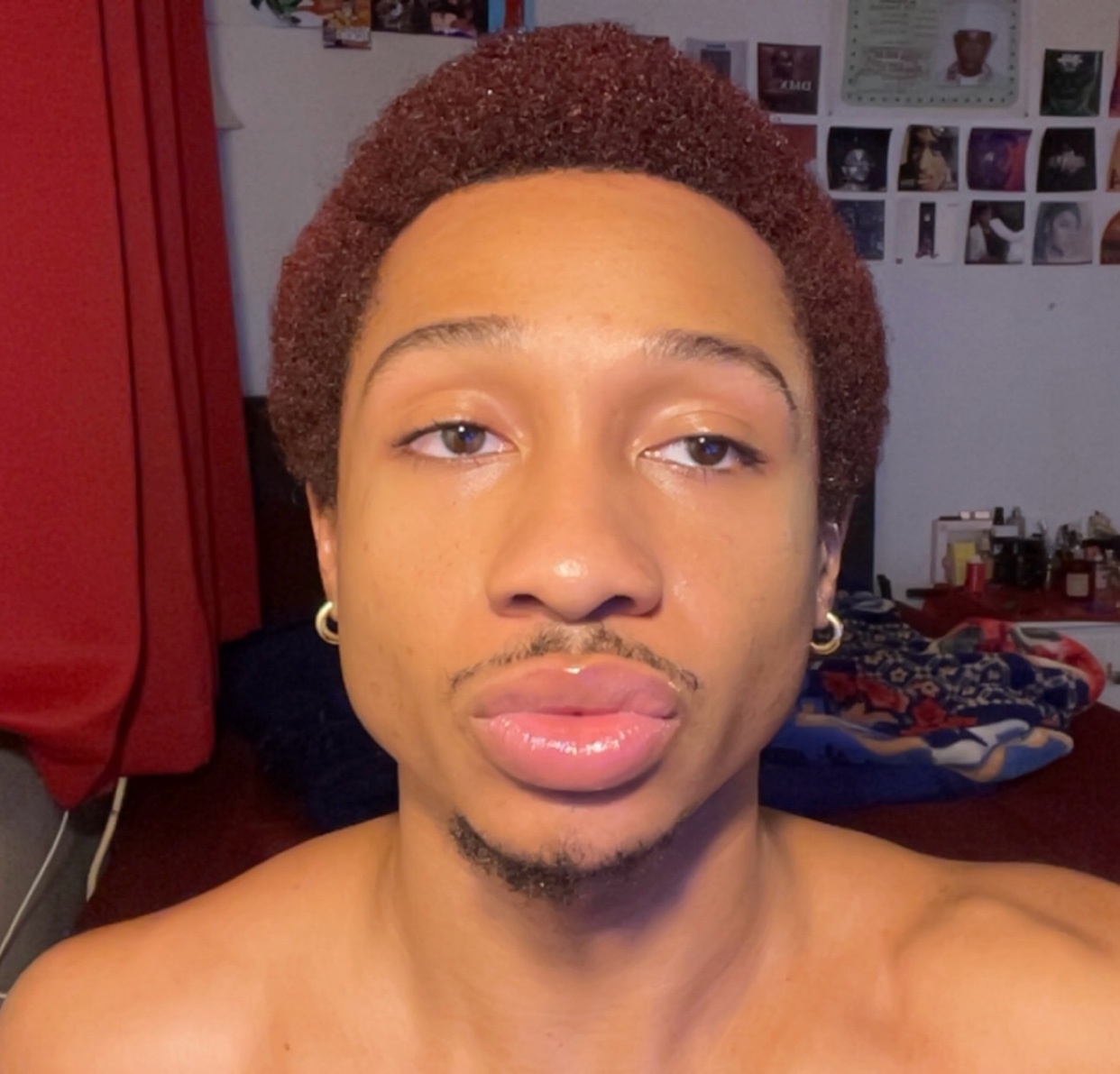 A shirtless man takes a selfie. He has curly dark hair and a mustache.