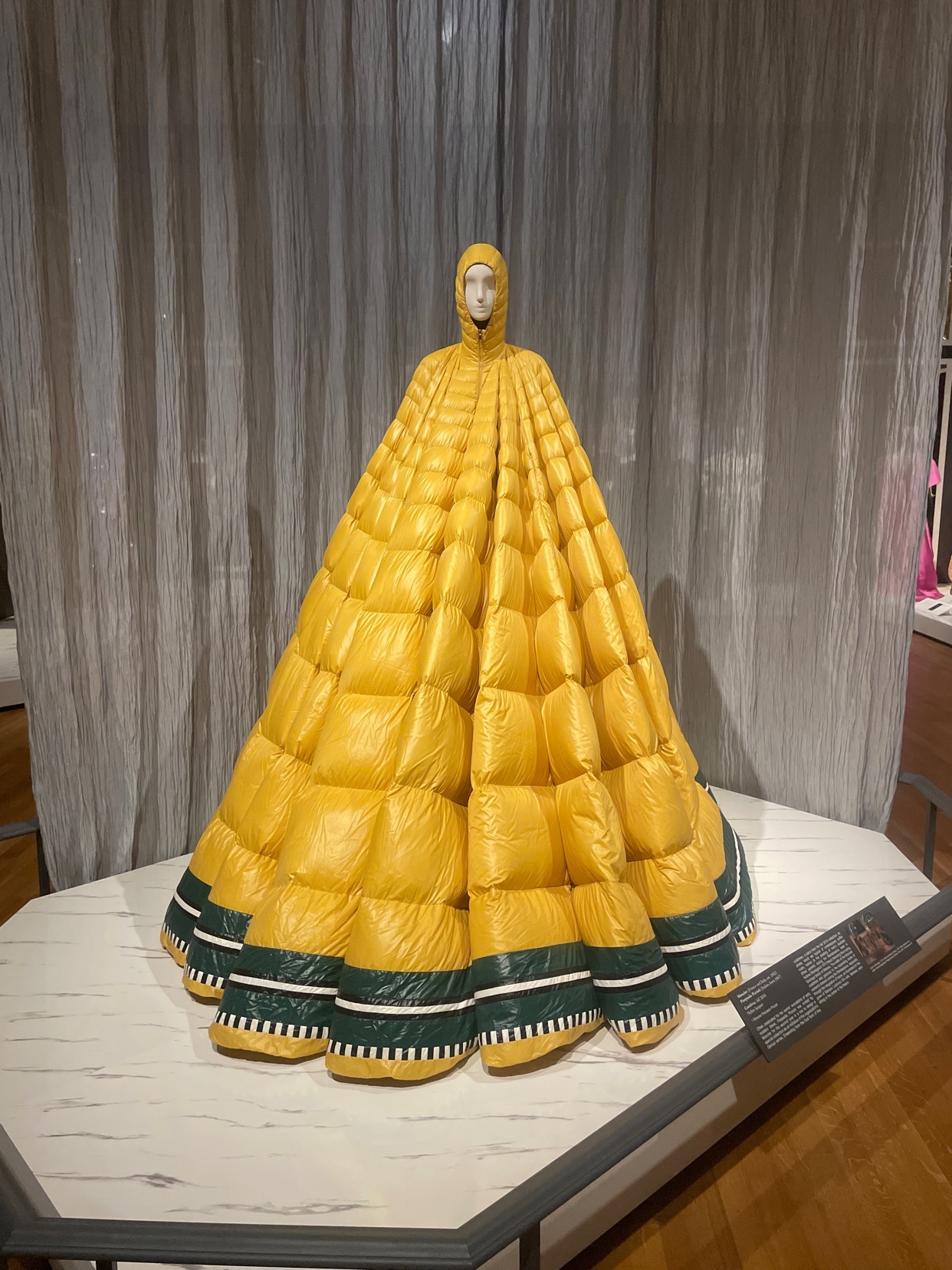A striking yellow dress on display. The dress has a unique quilted design and is part of a fashion exhibition.