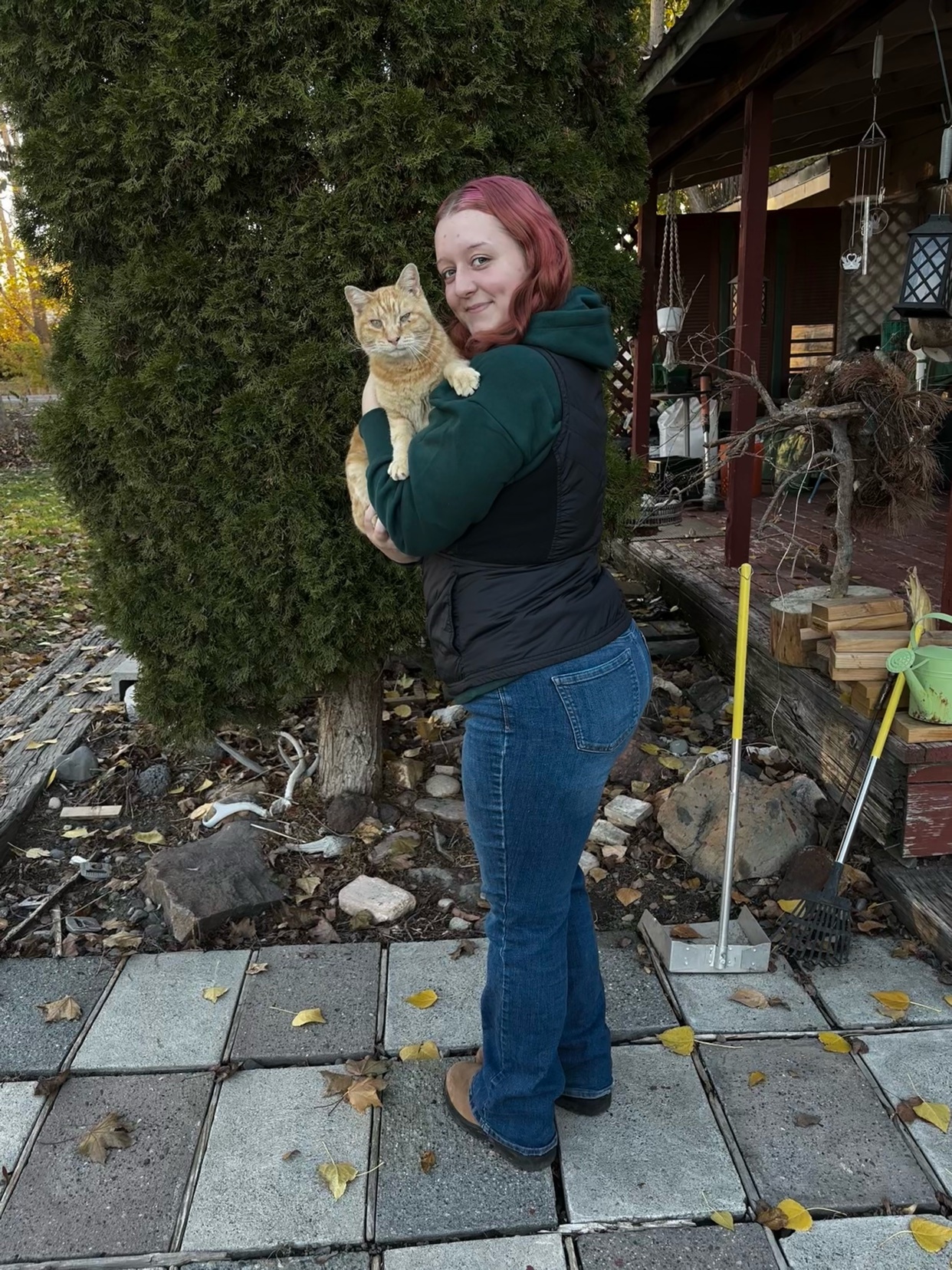 A woman holds a cat in her arms while standing outside. The woman is smiling and looking at the camera.