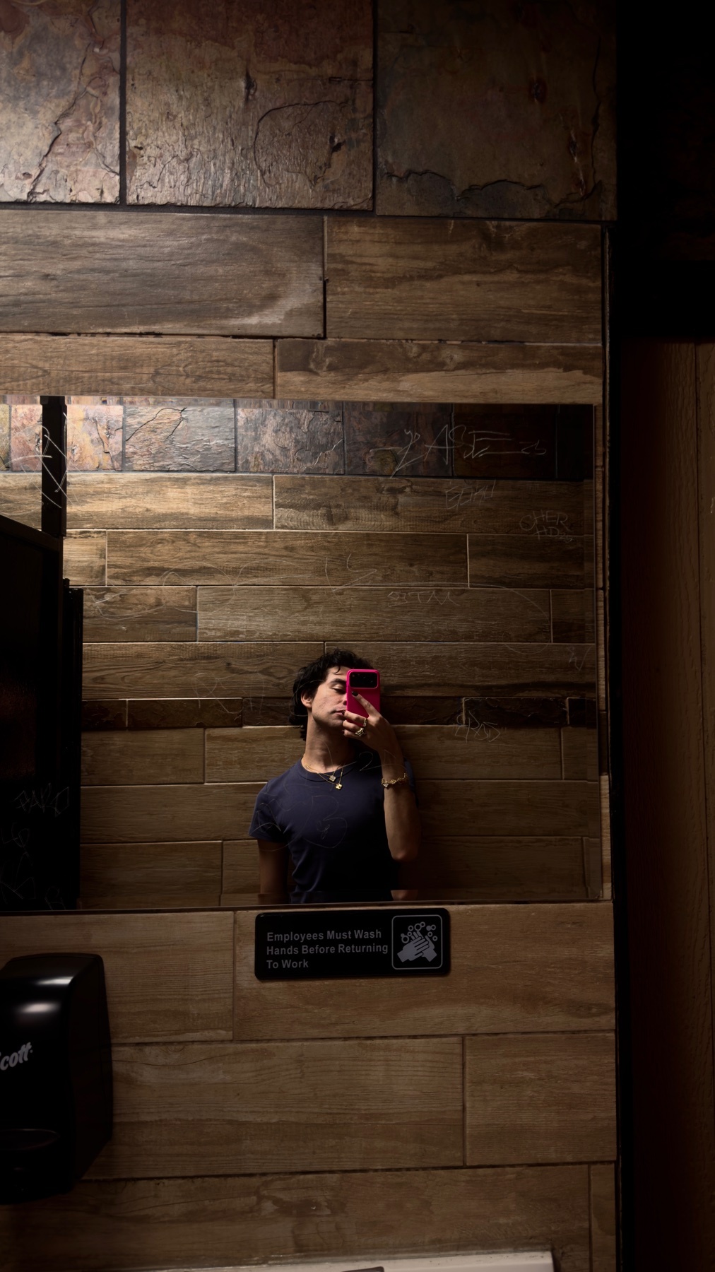 A man takes a mirror selfie in a bathroom. The bathroom features a unique wood and stone tile design.