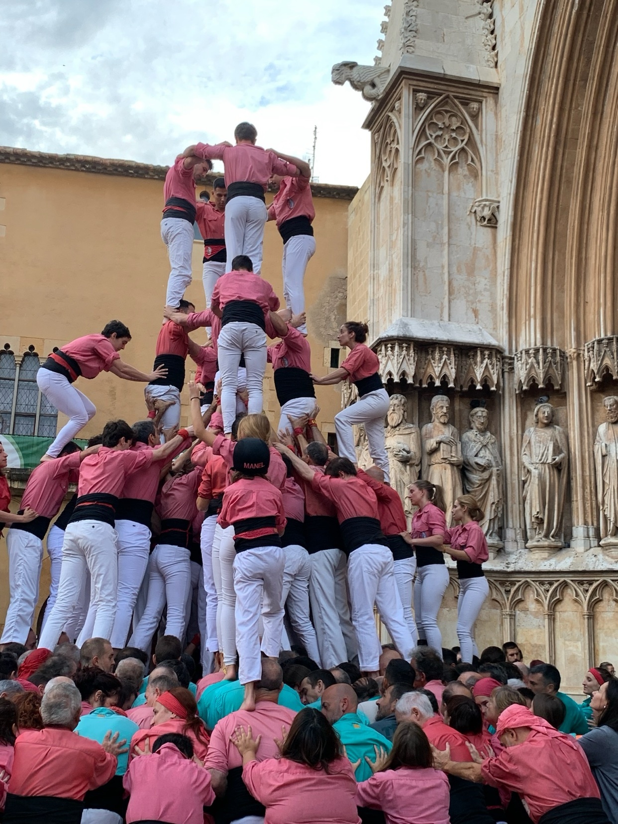 A human tower, or castells, is constructed by a group of people. The tower is built in front of a building with architectural details.