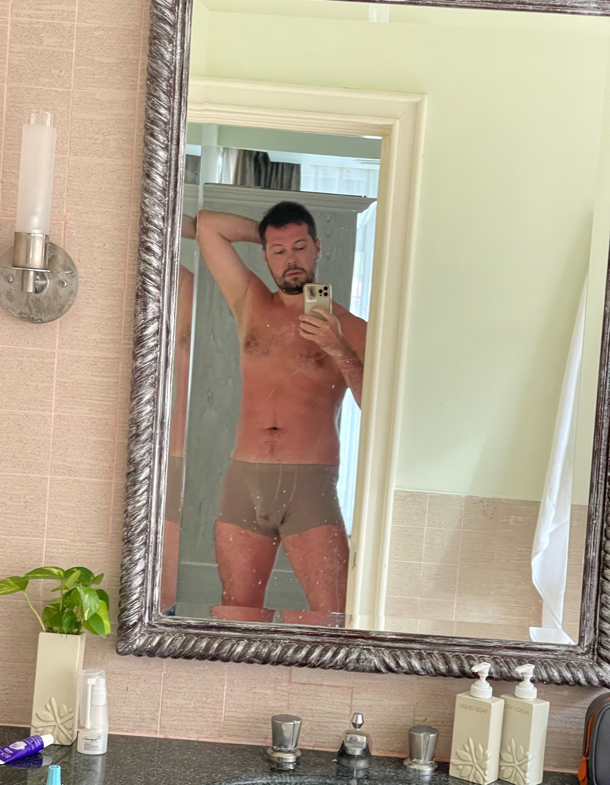 A man takes a mirror selfie in his underwear. He is shirtless and has a tan.