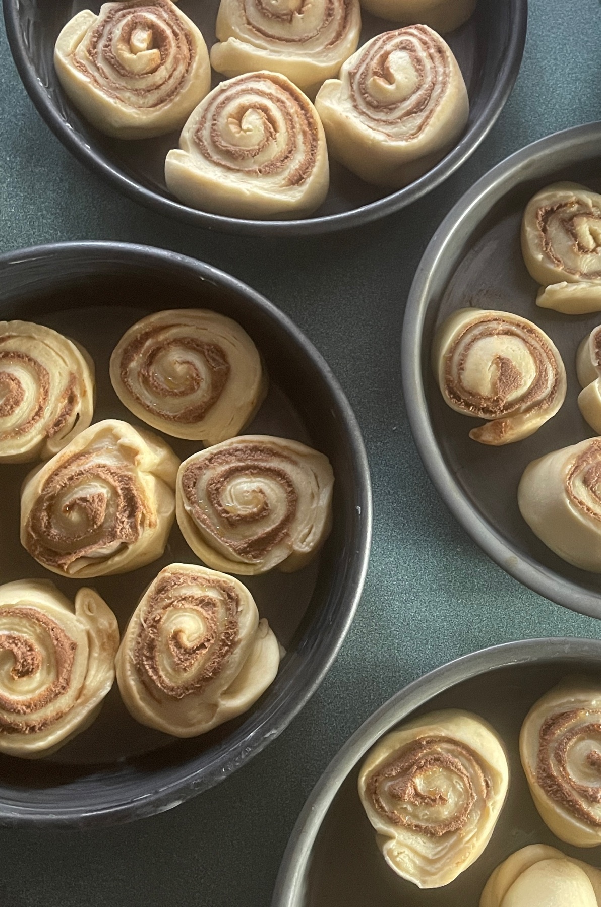 Overhead shot of several pans filled with uncooked cinnamon rolls. The rolls are arranged in circular patterns, ready for baking.