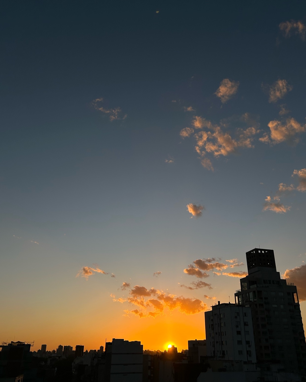 A beautiful sunset over a cityscape. The sky is filled with clouds, and the sun is setting behind the buildings.