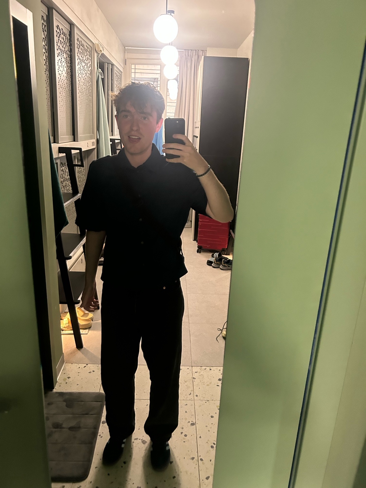 A man takes a mirror selfie, showcasing his all-black outfit. The photo captures his style and the details of his attire.
