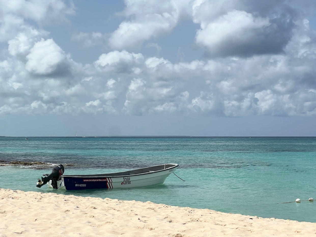 A small boat floats in the turquoise water near a sandy beach. The sky is filled with fluffy white clouds.