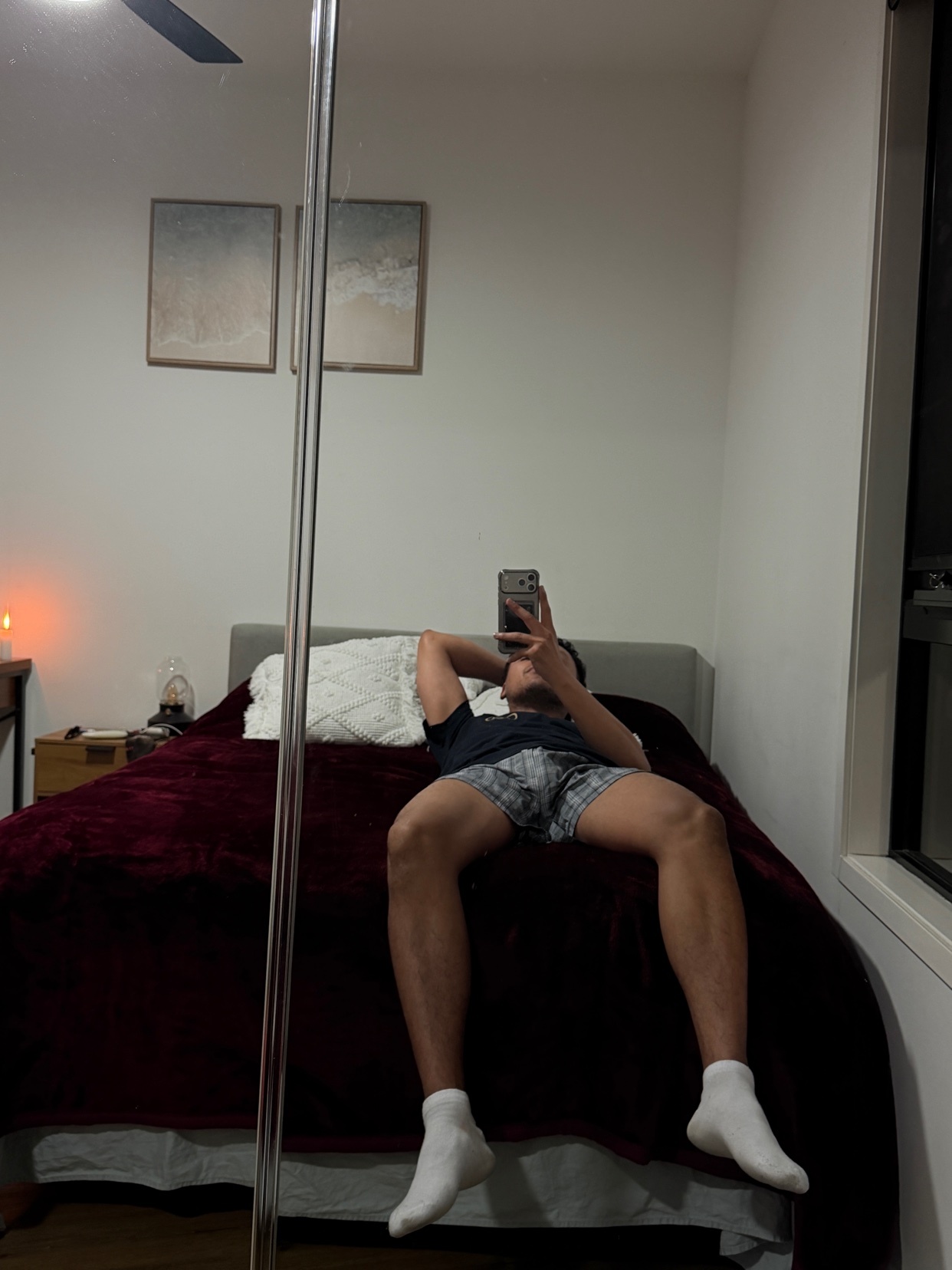 A man takes a mirror selfie while lying on a bed in a bedroom. He is wearing pajamas and white socks.
