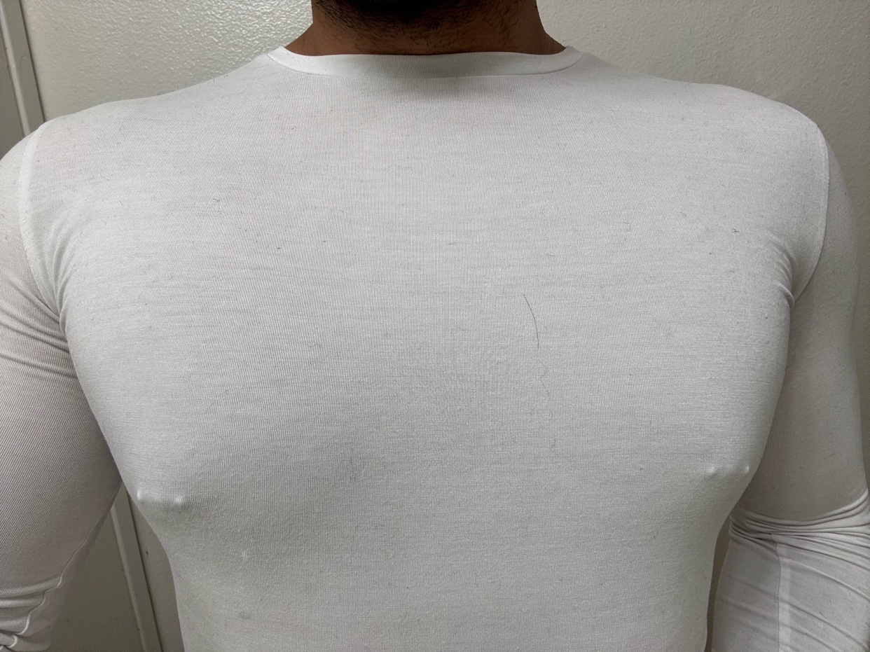 A man is shown from the chest up, wearing a white long-sleeved shirt. The image focuses on the man's physique.