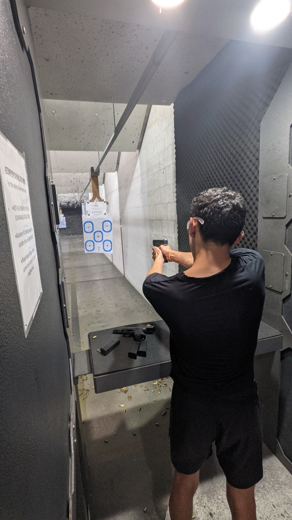 A man is at a shooting range, aiming a handgun at a target. The photo captures the indoor setting and the man's focus on the target.