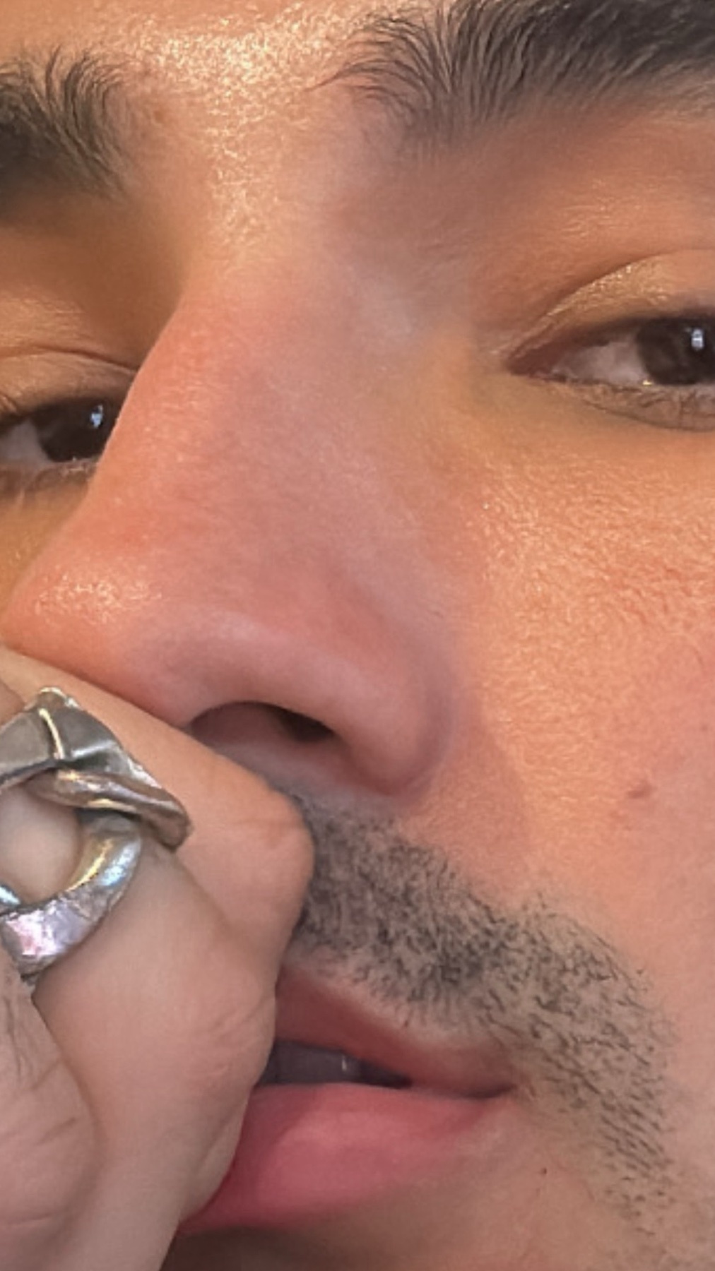 A close-up portrait of a man's face, with a focus on his eyes and facial features. He is wearing a ring on his finger.