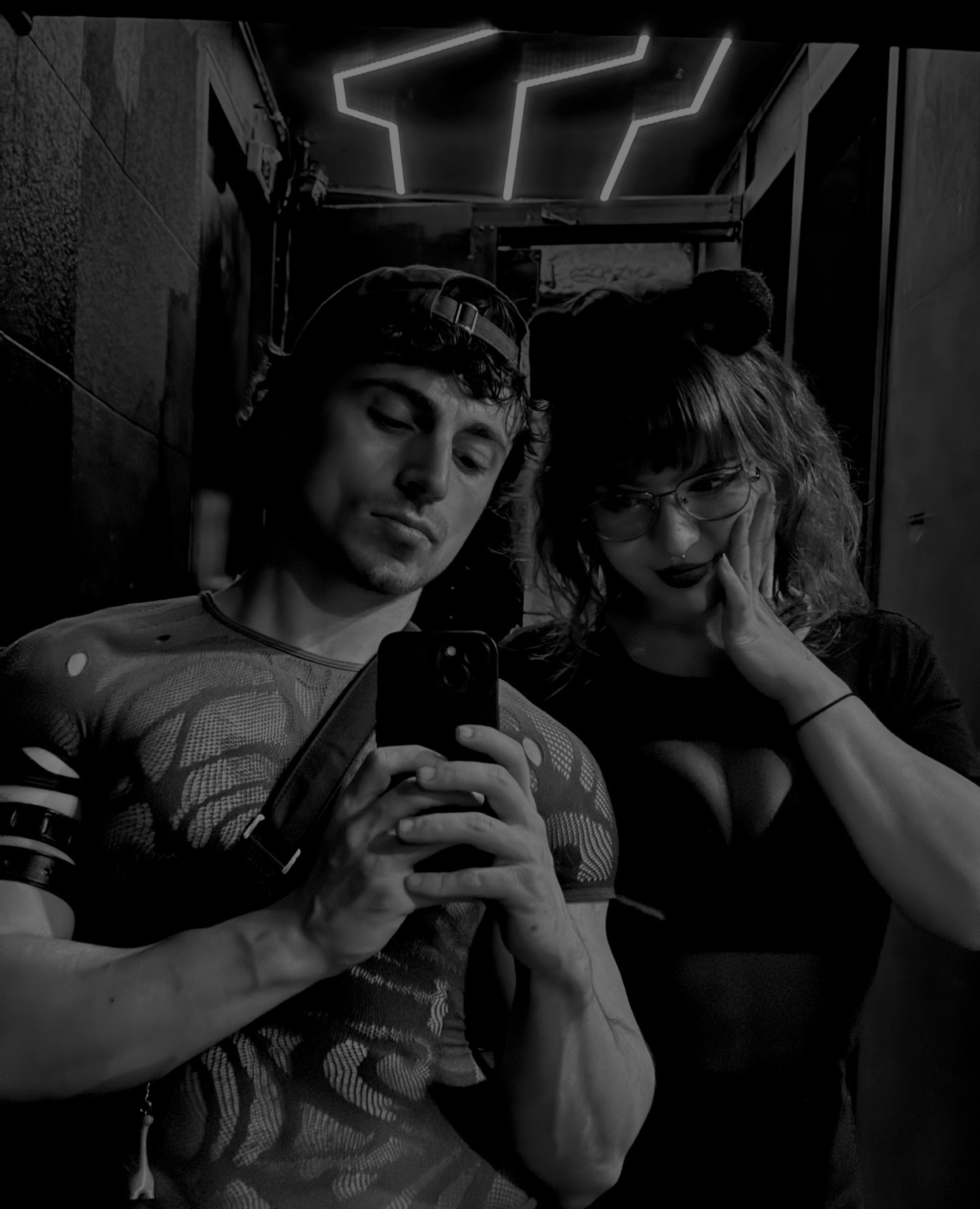 A black and white selfie of a couple. The man is shirtless and the woman is wearing a low-cut top.