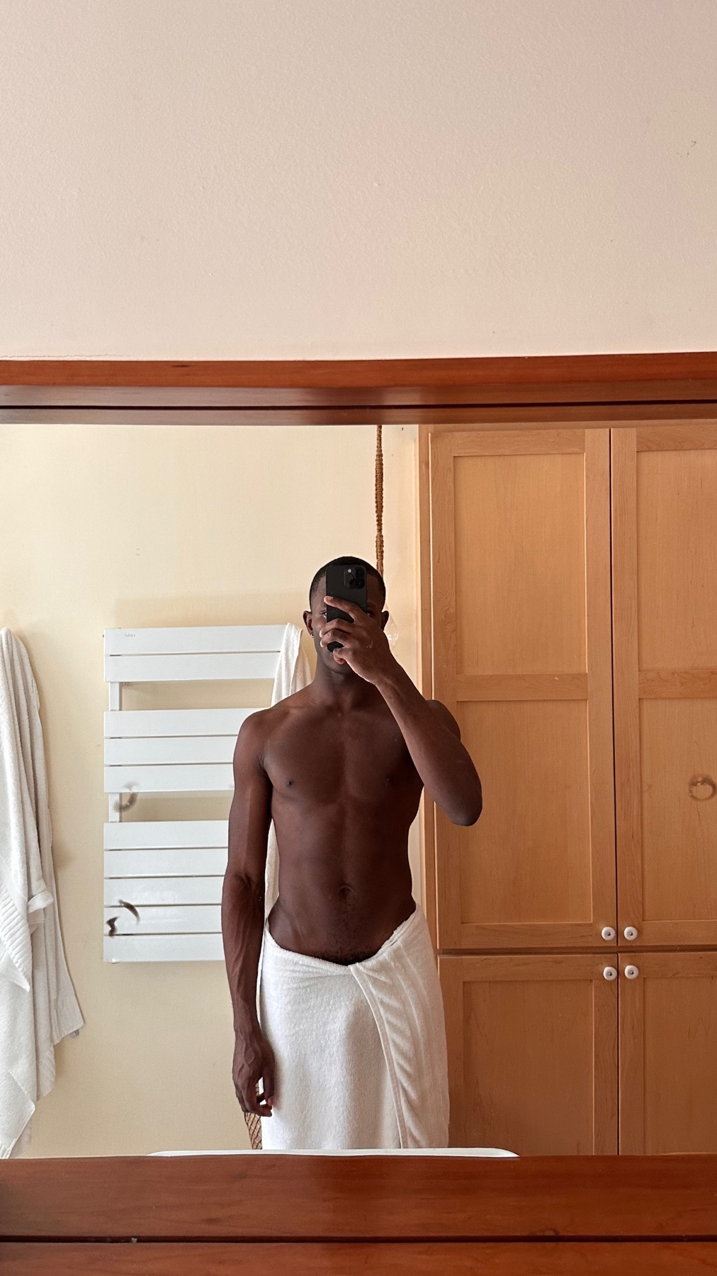 A man takes a mirror selfie, shirtless and wrapped in a towel. The photo highlights his physique in a bathroom setting.