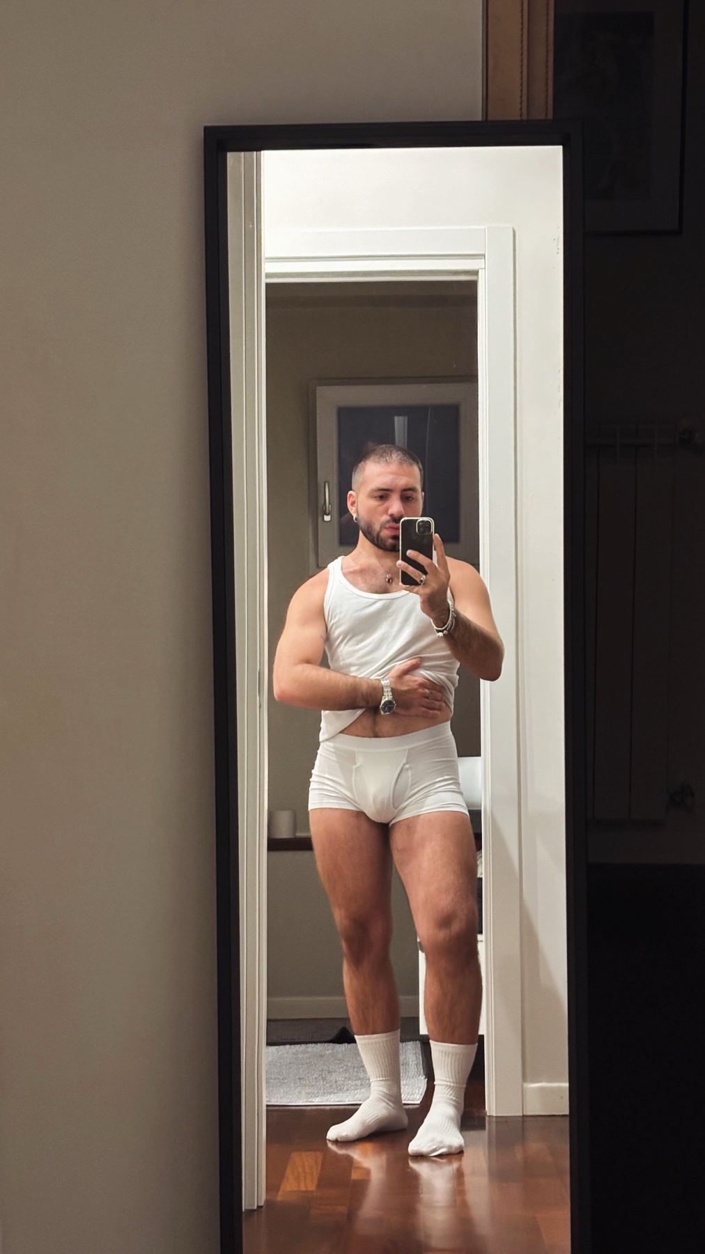 A man takes a mirror selfie, shirtless and in his underwear. He is flexing his muscles.