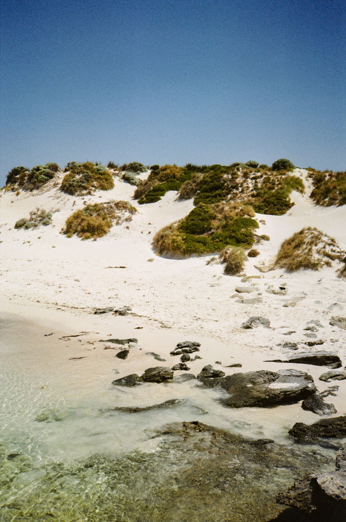 A beautiful beach scene with white sand, clear water, and a blue sky. The image captures the natural beauty of the coast.