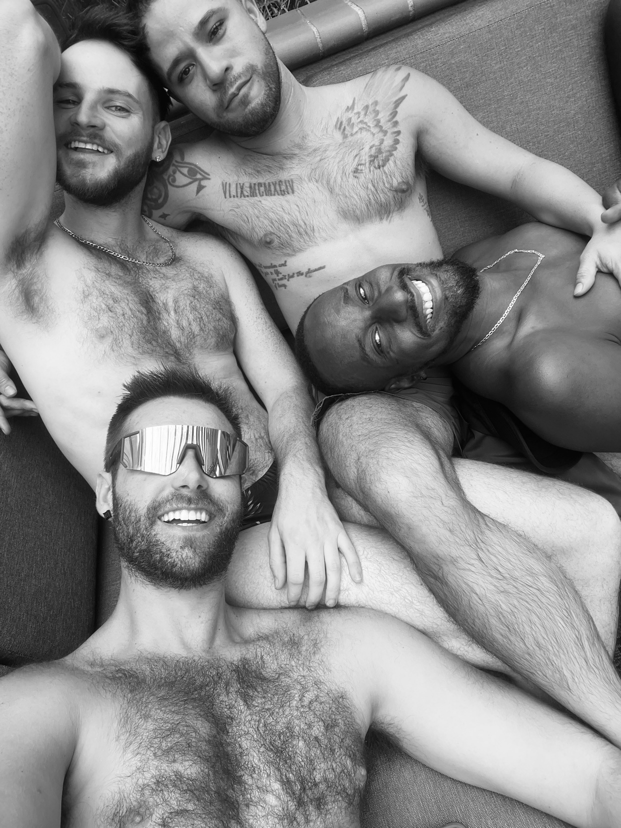 A black and white photo of four shirtless men posing together. They are smiling and appear to be enjoying themselves.