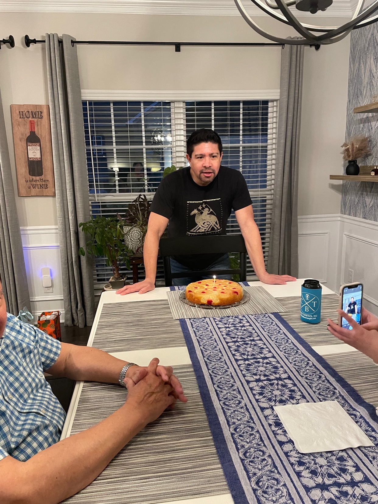 A man stands at a table with a birthday cake. The photo captures a birthday celebration in an indoor setting.