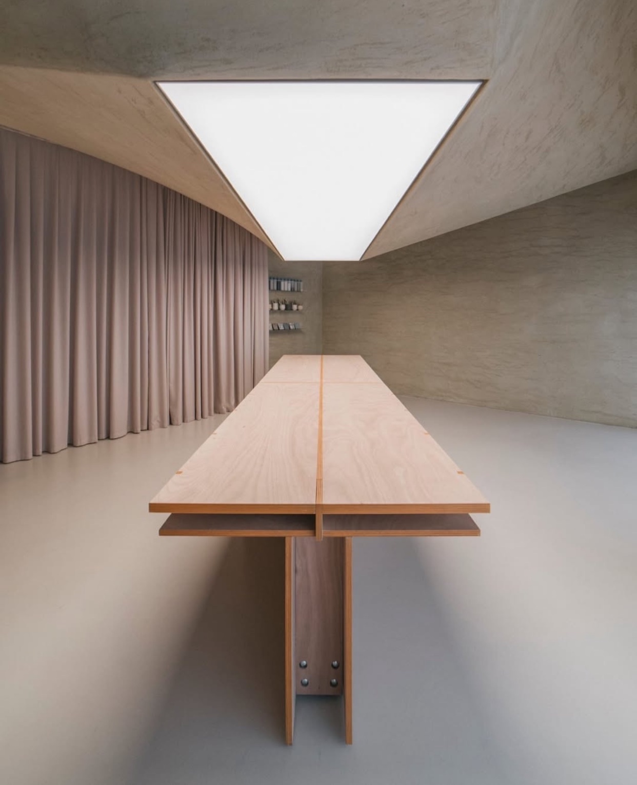 A modern, minimalist interior with a long wooden table and a large, rectangular light fixture. The space is characterized by clean lines, neutral tones, and a sense of spaciousness.