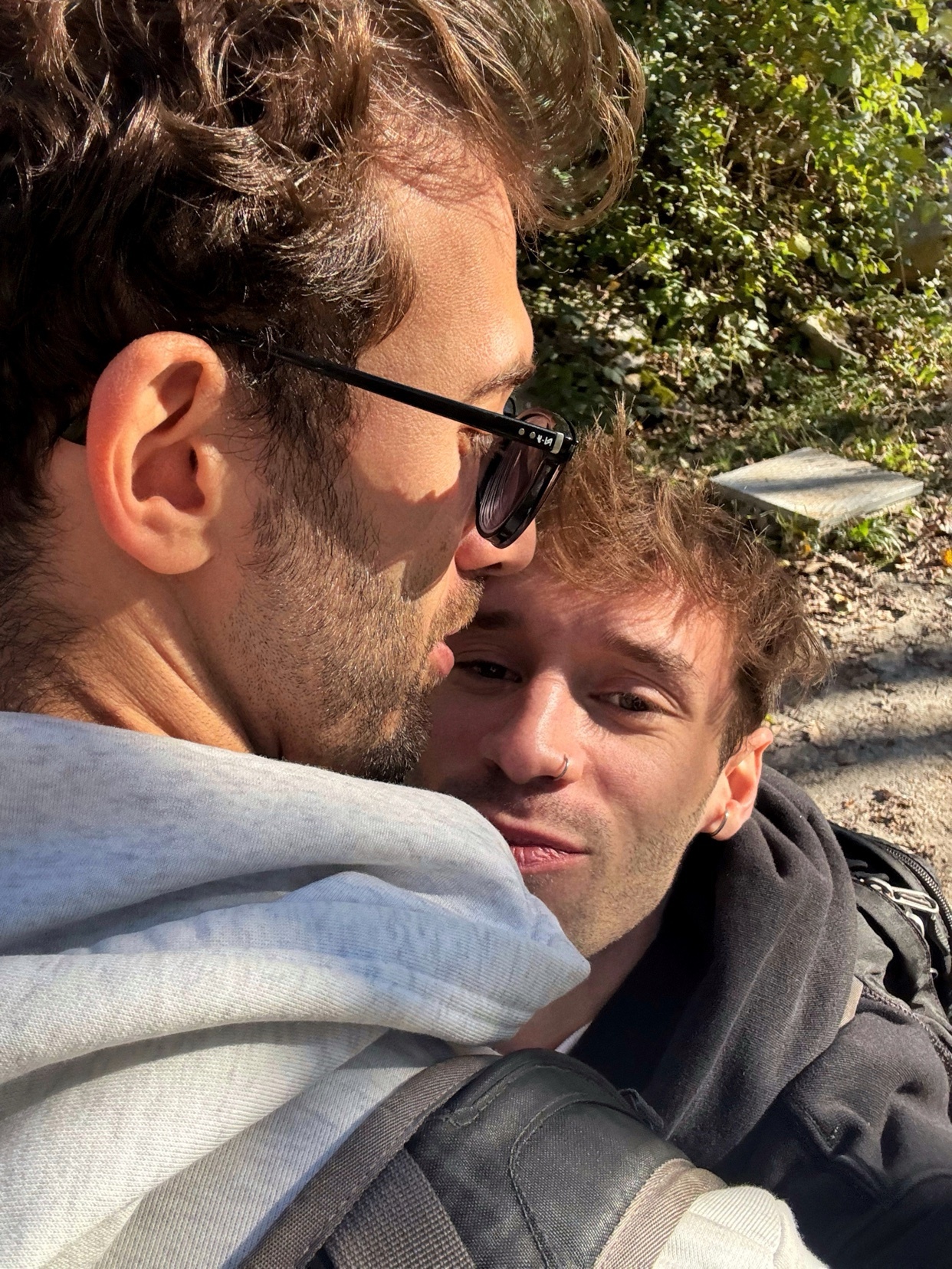 A close-up photo of a couple embracing outdoors. The men are smiling and appear to be in love.