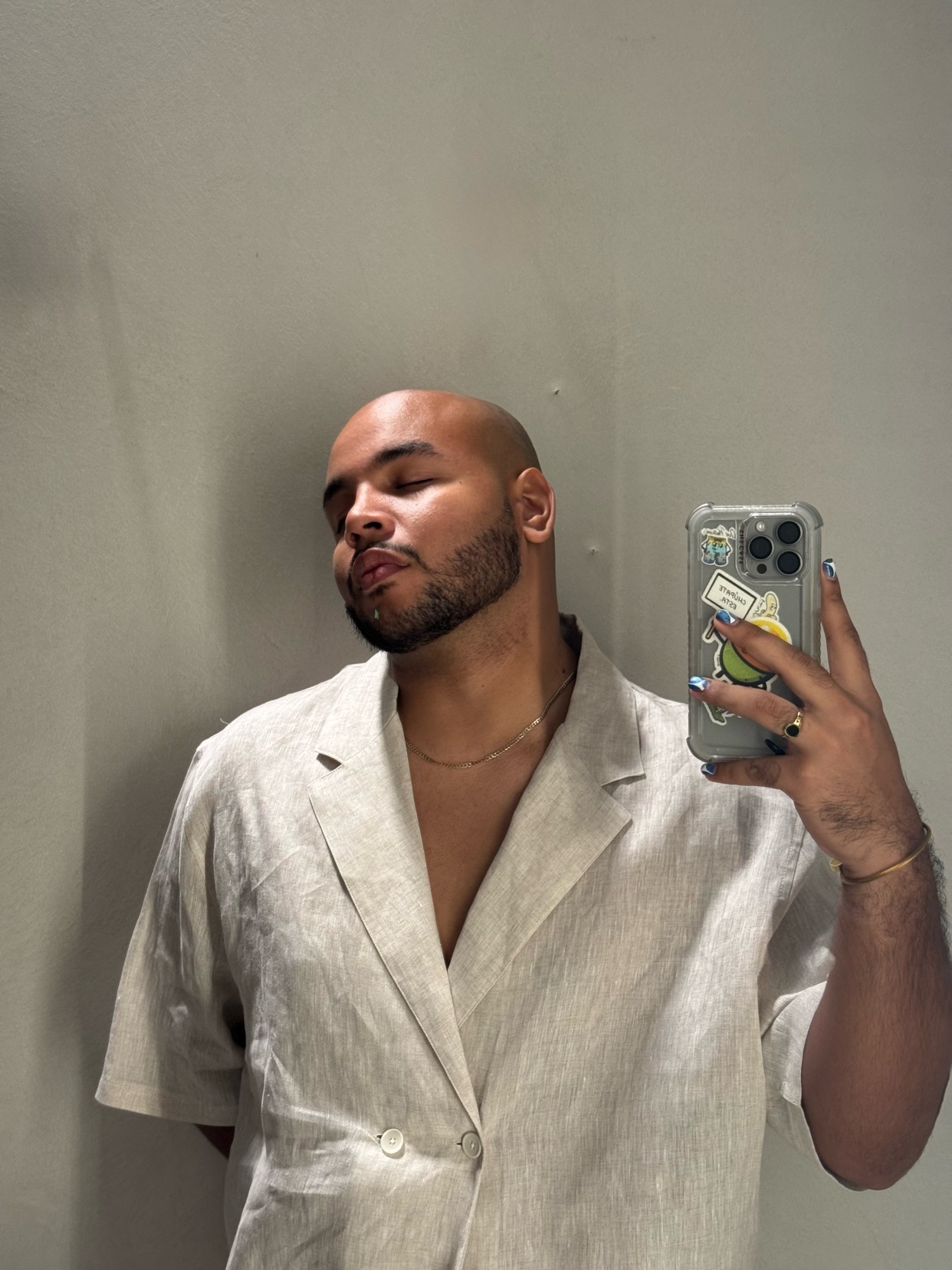 A man takes a selfie, showcasing his style. He is bald with a beard and wearing a shirt and gold chain.