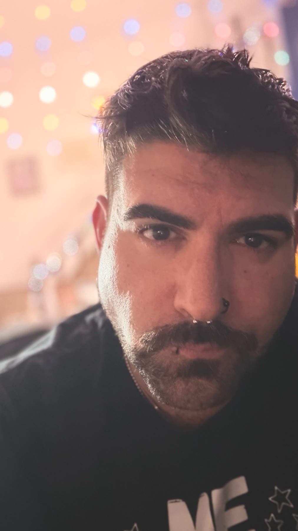 A close-up portrait of a man with dark hair and a mustache. He is looking directly at the camera.